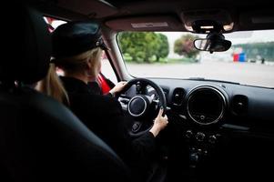 Portrait of beautiful blonde sexy fashion woman model in cap and in all black with bright makeup sit and drive red city car. photo