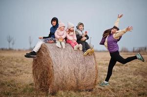 Four kids with mother having fun on haycock at field. photo