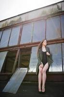 Sexy model girl wit long legs at black lingerie outfit body swimsuit combidress and jacket posed at the roof of abadoned industrial place with windows. photo