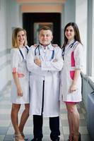 Two beautiful female doctors and one male in white coats posing in the hospital with stethoscope. photo