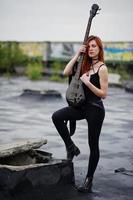 Red haired punk girl wear on black with bass guitar at the roof. photo