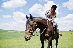 Young pretty girl riding a horse on a field at sunny day. photo