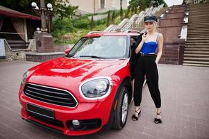 Portrait of beautiful blonde sexy fashion woman model in cap and in all black with bright makeup near red city car. photo