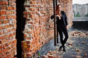 Red haired punk girl wear on black at the roof against brick wall with iron ladder. photo