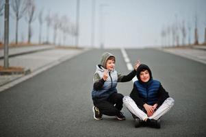 Brothers in hoodie sitting at center of road. photo