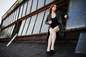 Sexy model girl wit long legs at black lingerie outfit body swimsuit combidress and jacket posed at the roof of abadoned industrial place with windows. photo