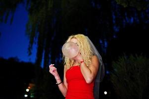 novia loca con vestido rojo y velo inflando condones en su despedida de soltera. foto