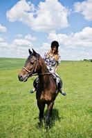 Young pretty girl riding a horse on a field at sunny day. photo