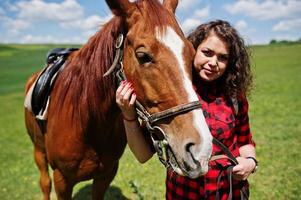 una joven bonita se queda con un caballo en un campo en un día soleado. foto
