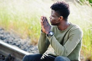 Cool black african american man sitting and posing on railway in the countryside. photo