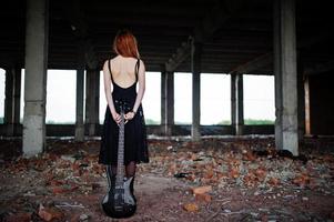 Red haired punk girl wear on black with bass guitar at abadoned place. Portrait of gothic woman musician. photo