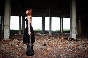 Chica punk pelirroja vestida de negro con bajo en un lugar abandonado. retrato de mujer gótica músico. foto