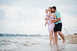 Summer vacations. Parents and people outdoor activity with children. Happy family holidays. Father, pregnant mother, baby daughter on sea sand beach. photo