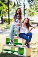 Two gorgeous young girls sitting on wooden boxes in the park on a sunny day. photo