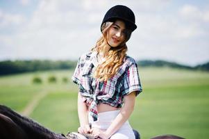 Young pretty girl riding a horse on a field at sunny day. photo