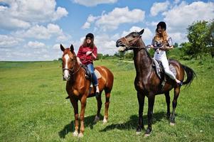 Tow young pretty girls riding a horses on a field at sunny day photo