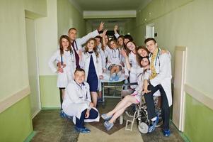 Crazy young doctors having fun by posing on a wheelchair in the hallway of hospital. photo