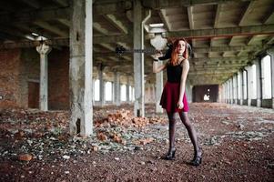 Red haired punk girl wear on black and red skirt, with bass guitar at abadoned place. Portrait of gothic woman musician. photo