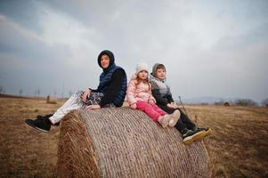 Three kids sitting on haycock at field. photo