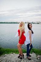 impresionante novia en vestido rojo posando con su dama de honor en la orilla del lago. foto