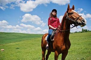 jovencita bonita montando un caballo en un campo en un día soleado. foto