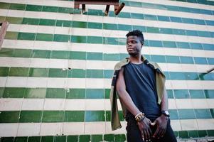 Attractive young african american guy in casual clothing standing next to the tiled wall. photo