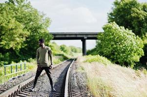 Cool black african american man walking and posing on railway in the countryside. photo