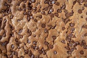 closeup of large chocolate chip cookie cake on rustic white background flat lay photo