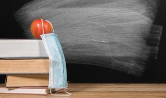 Back to virtual school background concept with stack of books and apple with face mask photo