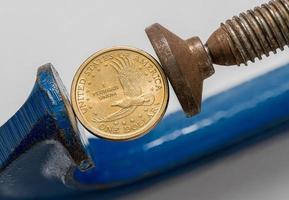 USA one dollar coin being squeezed between the solid jaws of a vise or vice photo