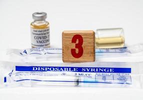 Concept for Covid-19 booster dose or shot using wooden three block with wrapped disposable syringes photo