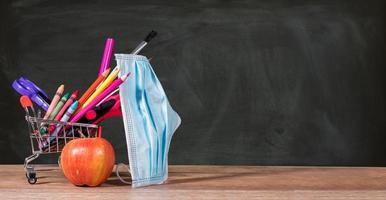 Back to school concept with pencils, crayons in shopping cart with apple with face mask photo