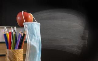 Back to virtual school background concept with stack of books, pencil, apple with face mask photo