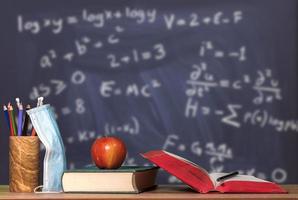 Back to virtual school background concept with stack of books, apple and face mask against math background photo