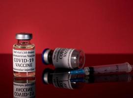 Covid-19 vaccine in vial with syringe reflected against red background photo