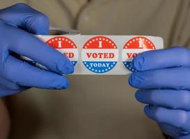 manos enguantadas sosteniendo un rollo de pegatinas o botones que voté hoy listos para el votante que votó en persona en las elecciones foto