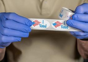 Gloved hands holding roll of I Voted stickers or buttons with USA flag ready for voter who voted in person in election photo