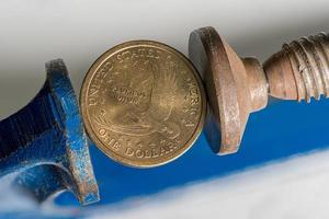 USA one dollar coin being squeezed between the solid jaws of a vise or vice photo