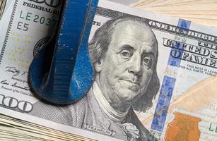 USA one hundred dollar notes being squeezed between the solid jaws of a vise or vice photo