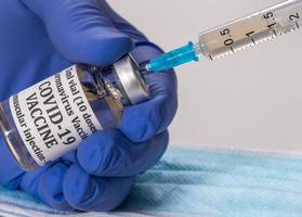 Close up of the end of the hypodermic syringe being inserted into bottle of vaccine photo