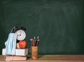 Back to virtual school background concept with stack of books, apple and alarm clock with face mask photo