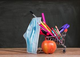Back to school concept with pencils, crayons in shopping cart with apple with face mask photo