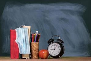 Back to virtual school background concept with stack of books, apple and alarm clock with face mask photo