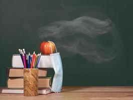 Back to virtual school background concept with stack of books and apple with face mask photo