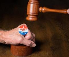 I voted by mail campaign button or sticker on hand with a gavel and mallet to illustrate lawsuits about voting photo