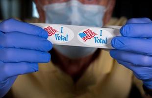 Gloved hands holding roll of I Voted stickers or buttons with USA flag ready for voter who voted in person in election photo