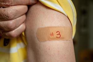 Senior man holding up shirt after third covid-19 vaccine injection photo