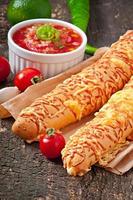 Salsa dip in bowl of bread and cheese sticks on wooden background photo