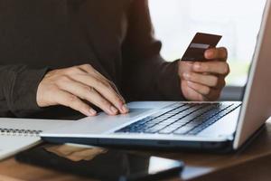 Businessman hand holding credit card with using laptop for online shopping while making orders at home. business, lifestyle, technology, ecommerce, digital banking and online payment concept. photo