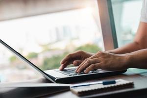 young man using laptop computer and mobile phone When looking for financial information in business, work at the desk. Writing with a pen, studying remotely from home and working from home. photo